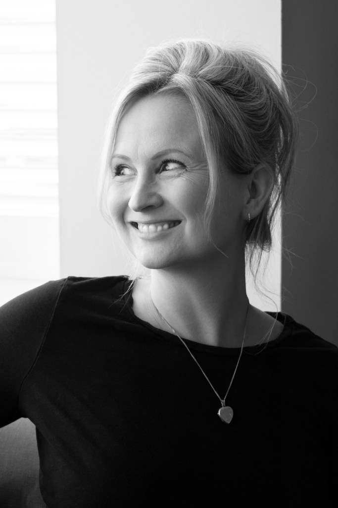 A black and white photo of Lucy wearing a black long sleeved t shirt with blonde hair tied up, looking slightly to the side